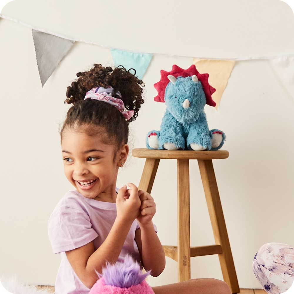 Image 105: Child sitting with Cute Weighted Lavender Scented Triceratops Stuffed Animal Heating Pad Warmies